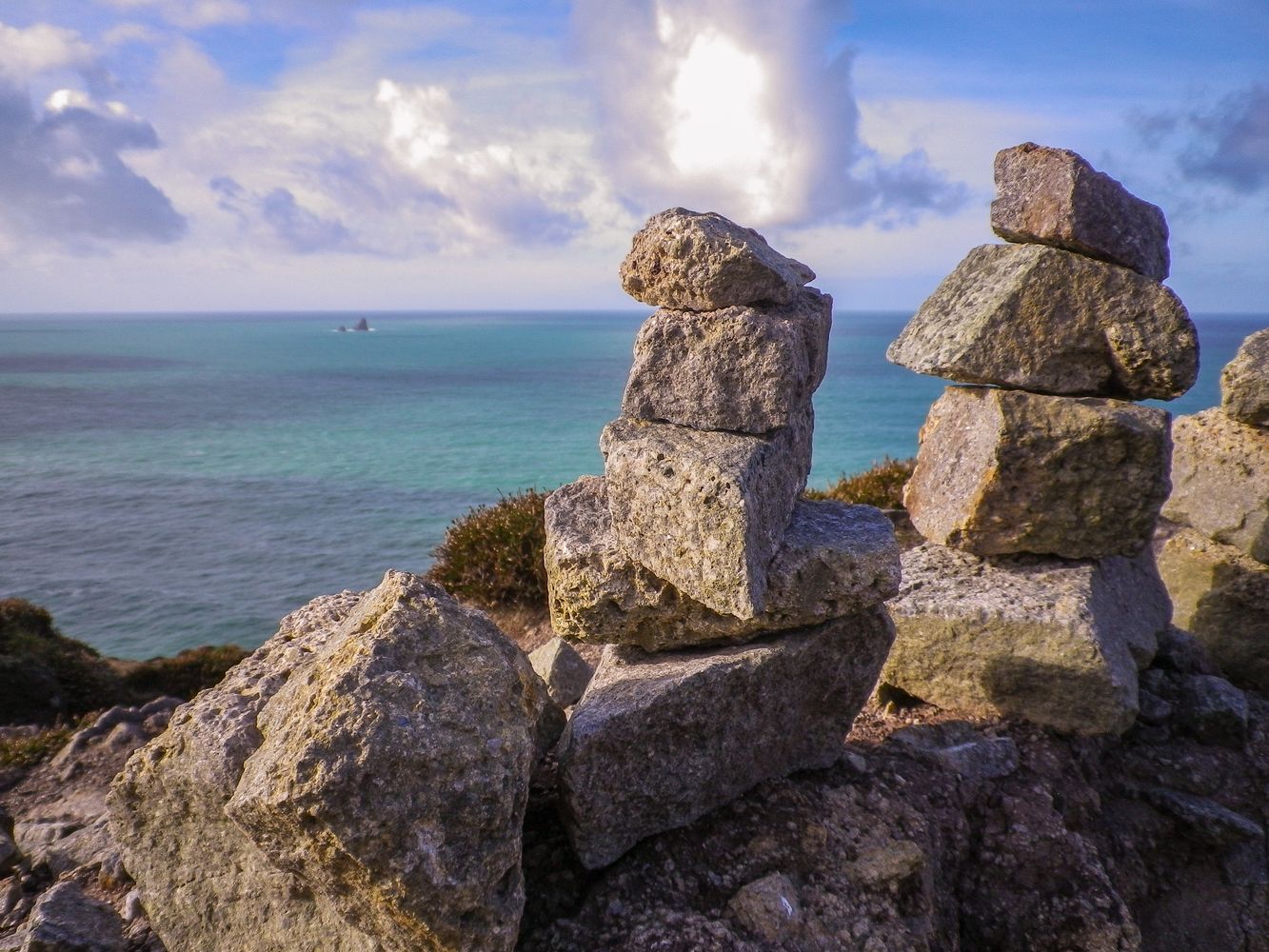 Balanced rock piles with background turquoise water of Atlantic Ocean and clouds at Cligga Head Mine, Cornwall.