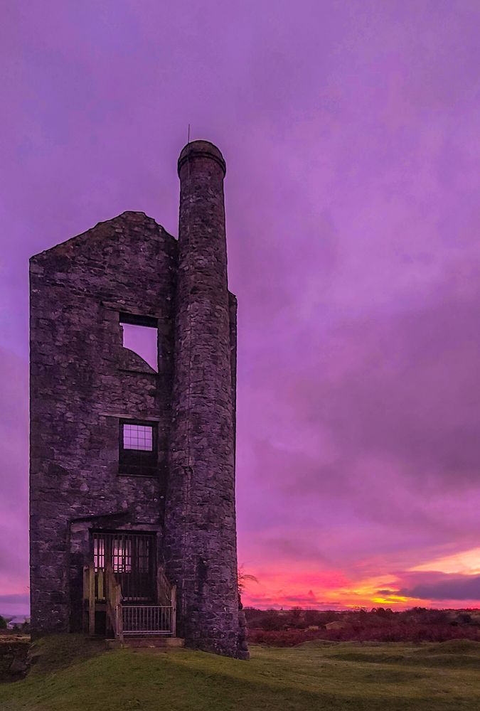 Mine engine house ruins on Bodmin Moor in Cornwall against a sunset with purple grey clouds